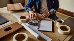 Marceneiro calculando o custo de uma coladeira de borda com calculadora e amostras de MDF